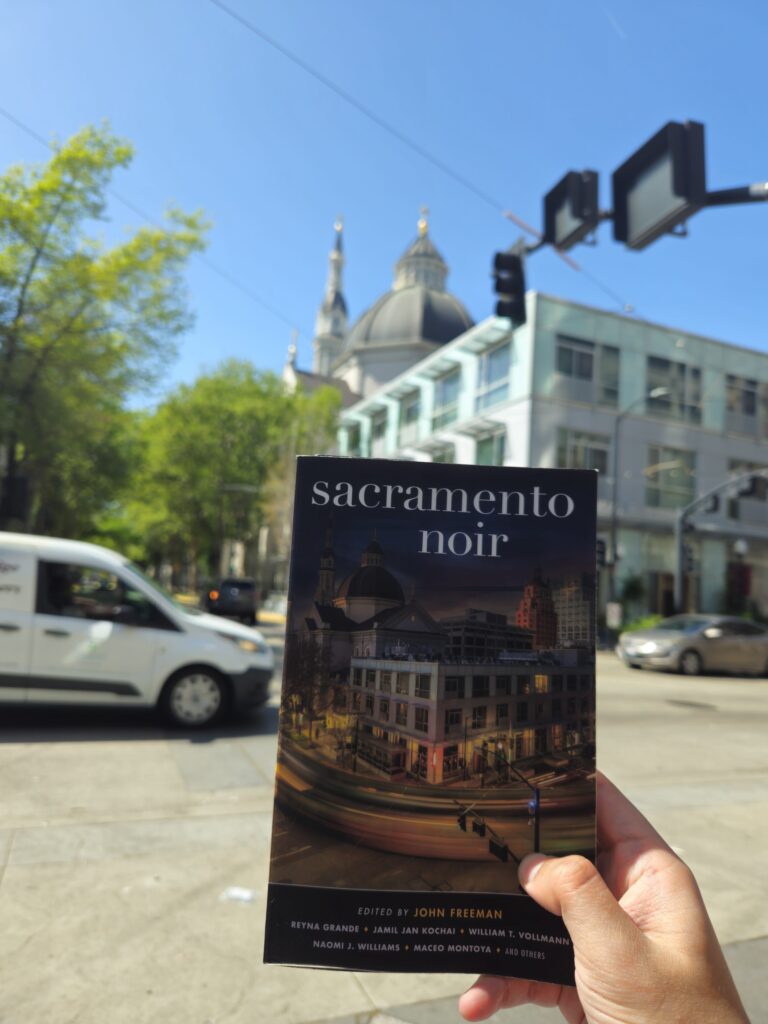 Photo showing Sacramento Noir held at the intersection of 11th and K Streets in downtown Sacramento, with the Safe Credit Union Convention Center in the foreground and the Cathedral of the Blessed Sacrament in the background. 🖼️ 6. Tower Bridge from the Old Sacramento Waterfront Trail 📍Old Sacramento Waterfront Trail Caption: Evening light stretches across the Old Sacramento Waterfront Trail toward the Tower Bridge — gold against the blue calm of the river. Description: Photo taken by Cameron Whitfield from the Old Sacramento Waterfront Trail, showing the Tower Bridge and the Ziggurat Building across the river. Long shadows from the railing mark the pavement as daylight fades. Alt Text: View from the Old Sacramento Waterfront Trail looking toward the Tower Bridge, with long shadows across the walkway beside the river and the Ziggurat Building in the distance. Optional Gallery Intro (for above the images) The stories in Sacramento Noir are fiction — but the city is real. These photos trace the landmarks and light that inspired them, from bookstore shelves to river trails, revealing a Sacramento that’s both familiar and elusive. Would you like me to output the WordPress-ready HTML gallery block version next (with and tags + alt text integrated)? That would make it a straight copy-paste section for your post editor.