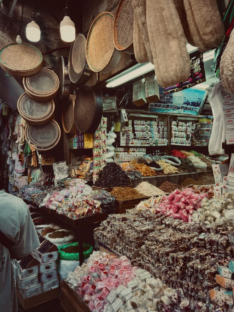 A bustling Palestinian souk with colorful textiles, lanterns, and market stalls lining a narrow street. Photo by Majd Glorio via Pexels.